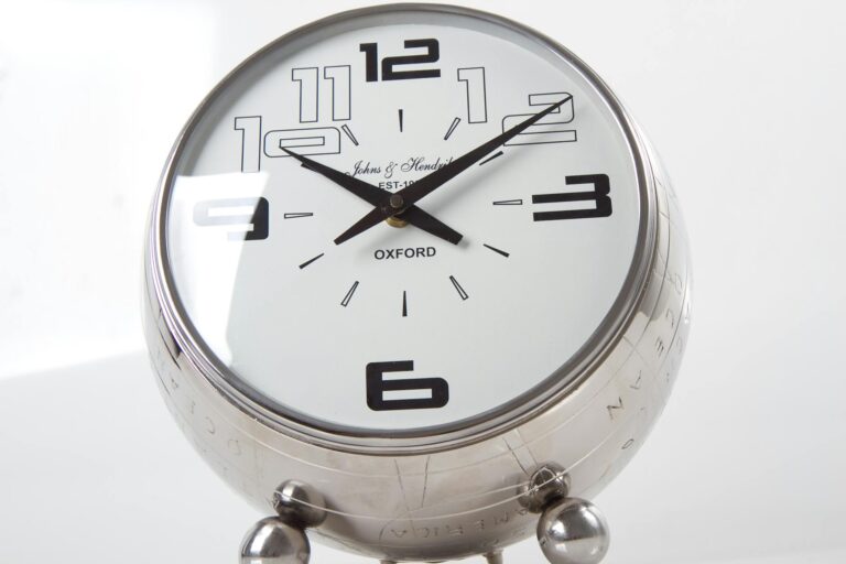 흰 배경 위에 놓인 크롬 재질의 탁상시계. 반짝이는 금속광과 단정한 숫자 디자인이 시간의 흐름과 효율성을 상징하는 장면.