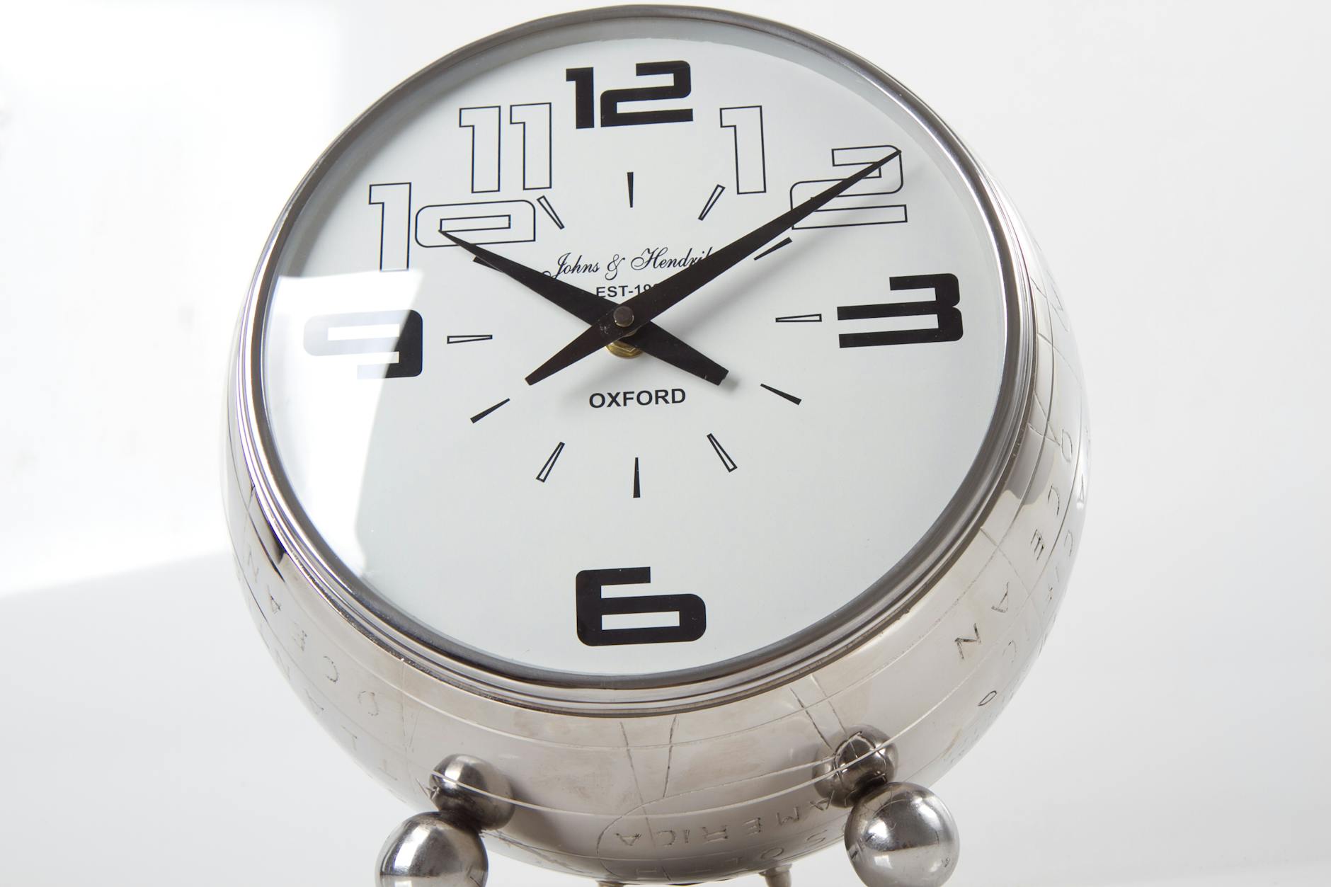 흰 배경 위에 놓인 크롬 재질의 탁상시계. 반짝이는 금속광과 단정한 숫자 디자인이 시간의 흐름과 효율성을 상징하는 장면.