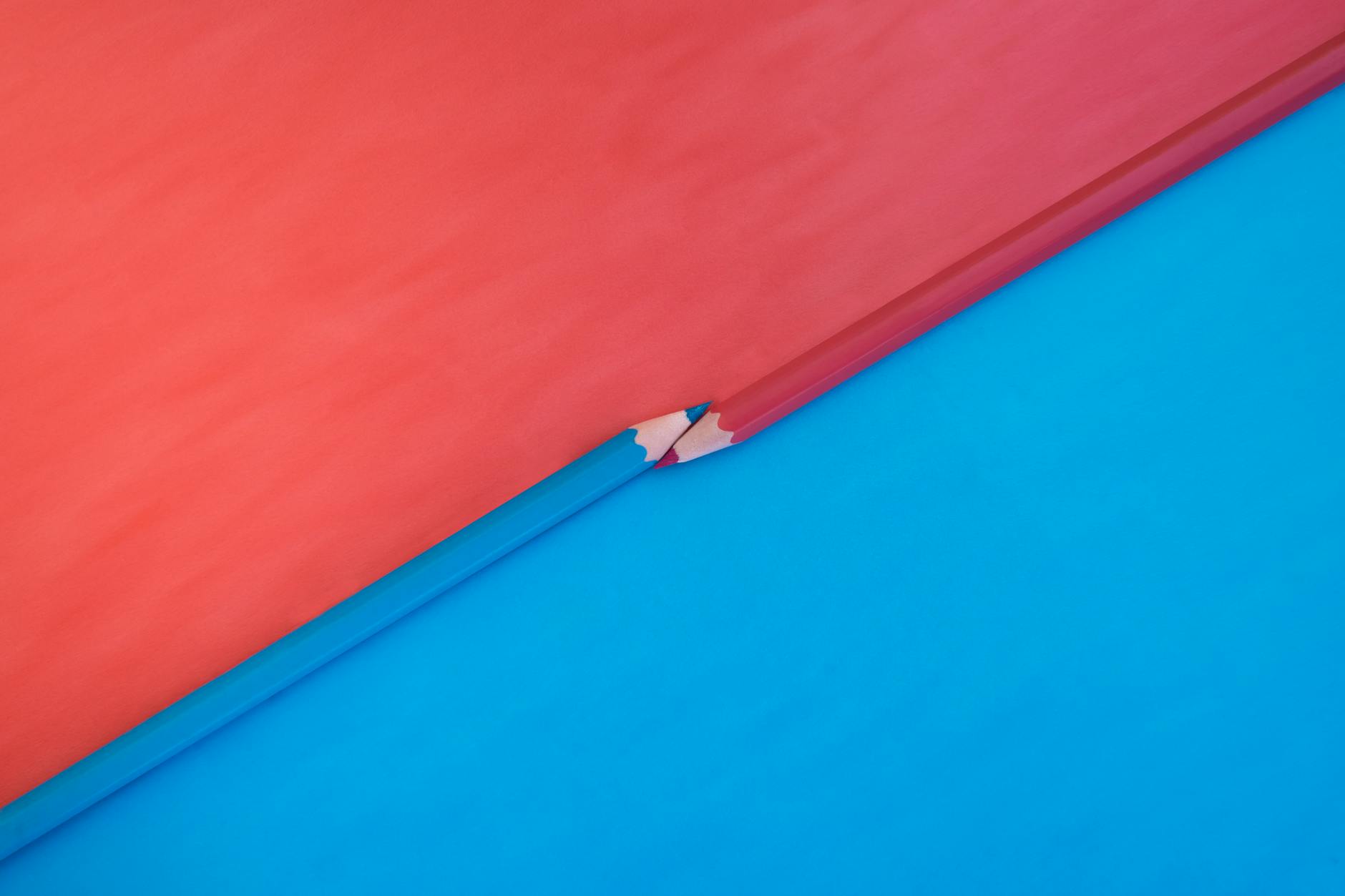 대비되는 빨강과 파랑 배경 위에 빨강과 파랑 연필 두 자루가 놓였다